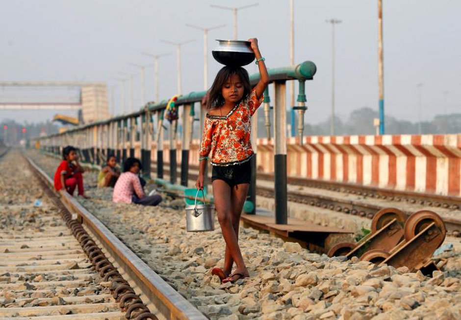 A girl carries utensils after filling them with water from a pipe that supplies water to trains at a railway station on the outskirts of Agartala