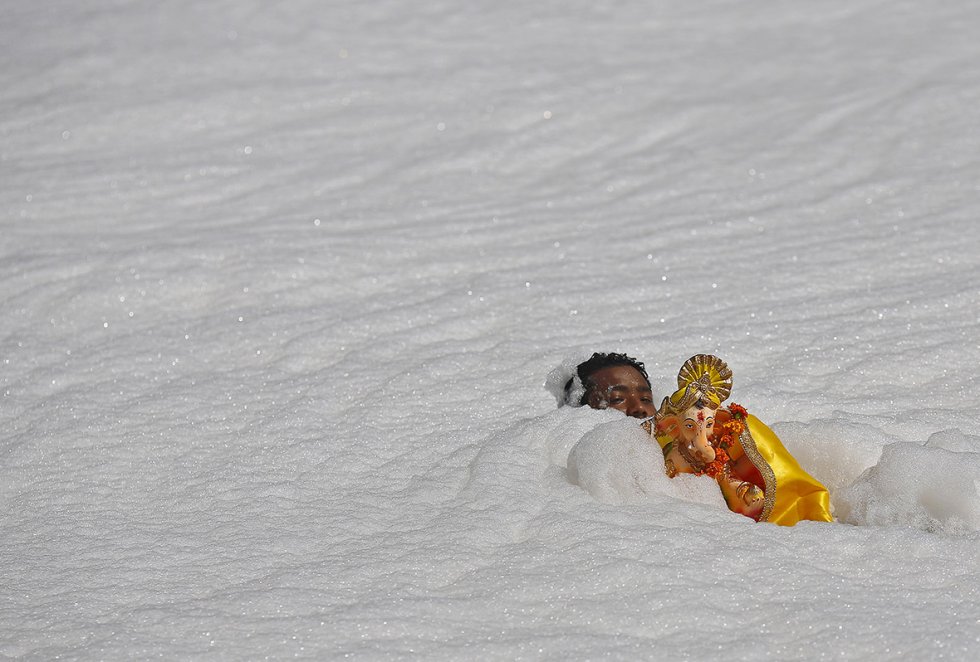 Man carrying Hindu god Ganesh statue through the polluted waters of the holy river Yamuna in New Delhi