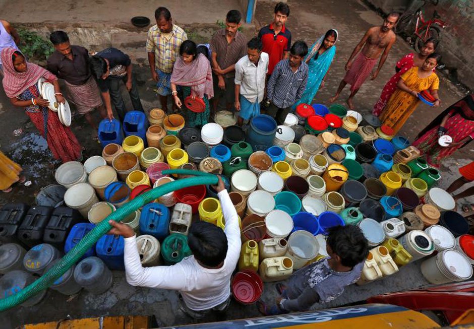 Residents wait as they get their containers filled with drinking water from a municipal tanker at a slum in Kolkata