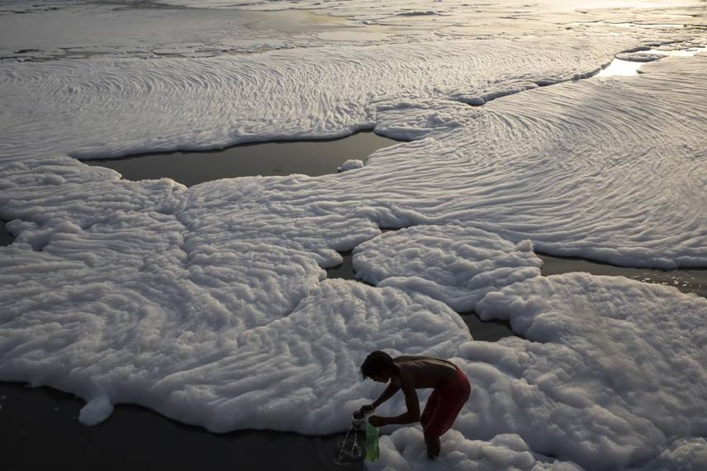 A man bathes and fills bottles with water from a foamy, polluted section of the Yamuna River on May 24 near the outskirts of New Delhi, India