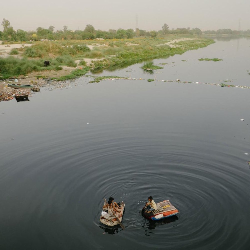 Children float on the polluted Yamuna River to look for any garbage that might be valuable