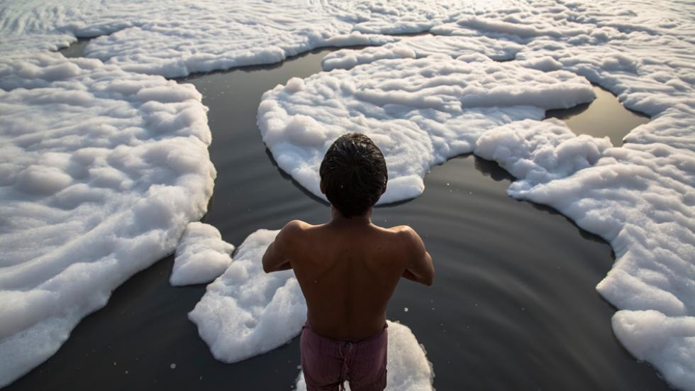 Indian men bathe in an industrial waste-foam polluted section of the Yamuna River