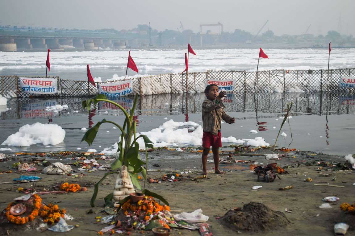 child plays with polluted foam after the overnight Chhath Puja celebrations wrapped up