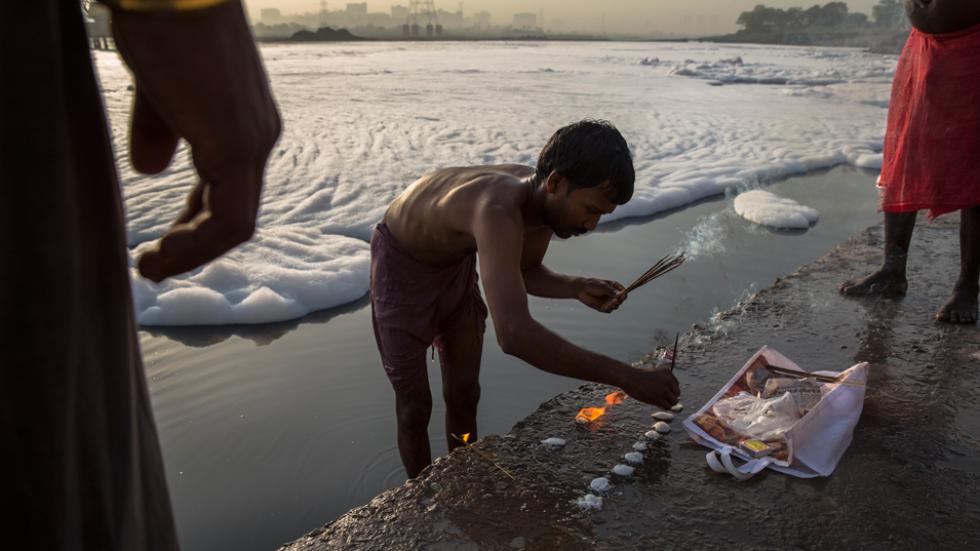 man makes an offering on the banks of an industrial waste-foam polluted section of the Yamuna River in New Delhi