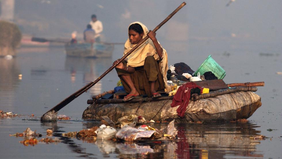 woman collects plastic refuse floating on the waters of The River Yamuna in New Delhi