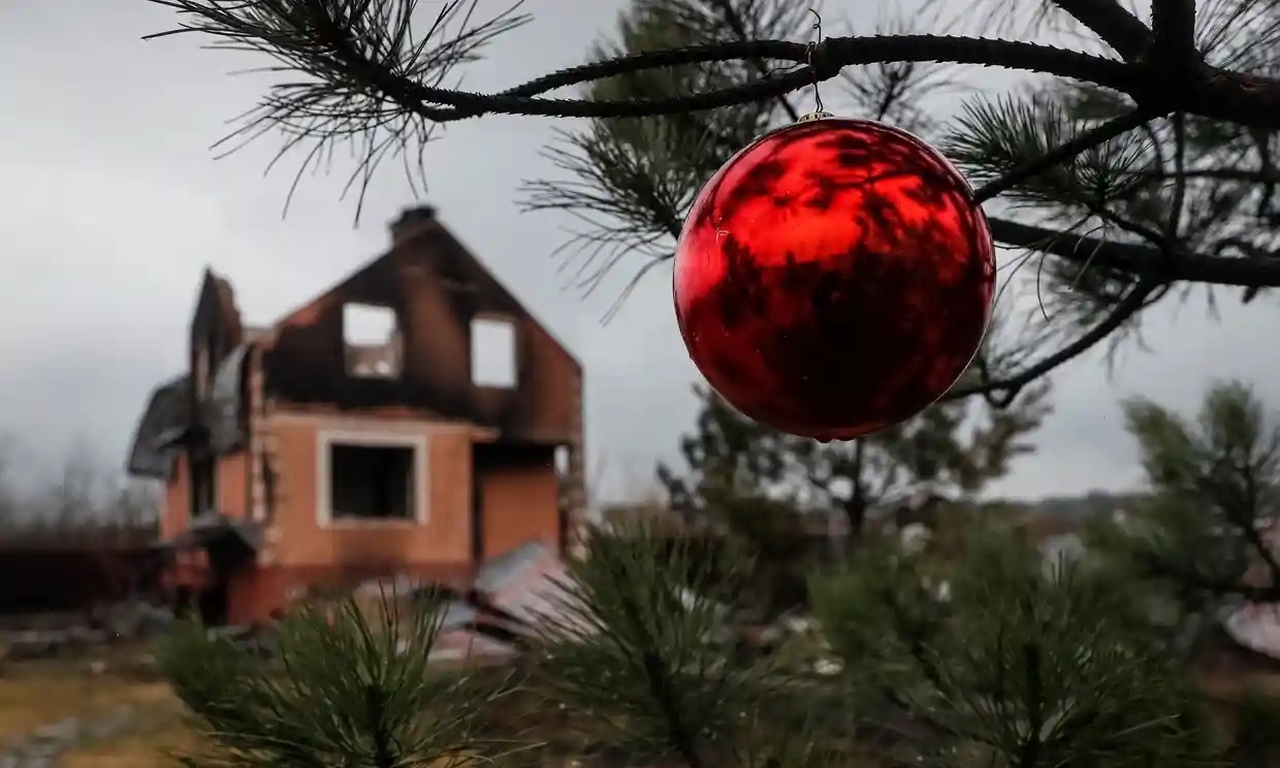 A Christmas bauble hanging on a branch in front of a destroyed house in Ukraine