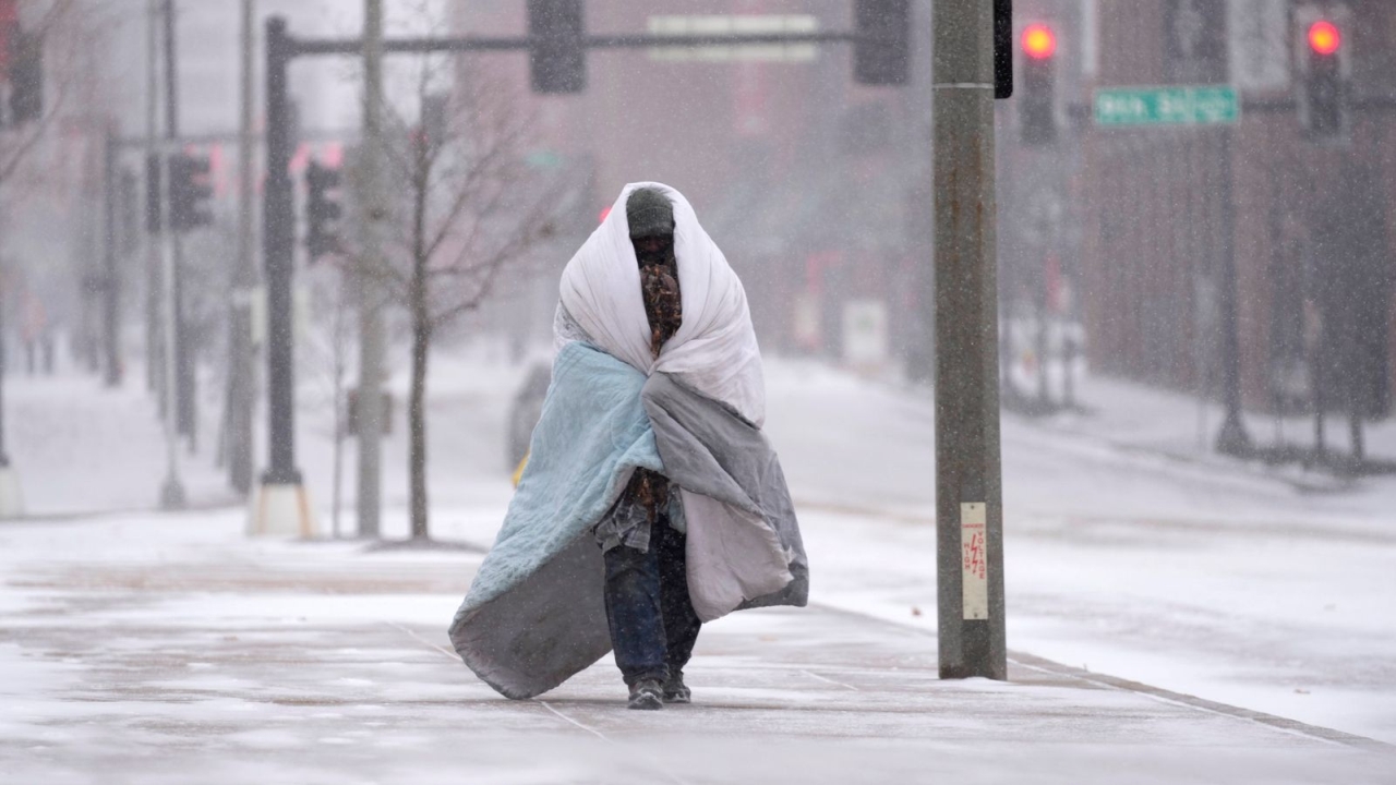Wrapped in a blanket, a man walks on a pavement as snow starts to fall in St Louis