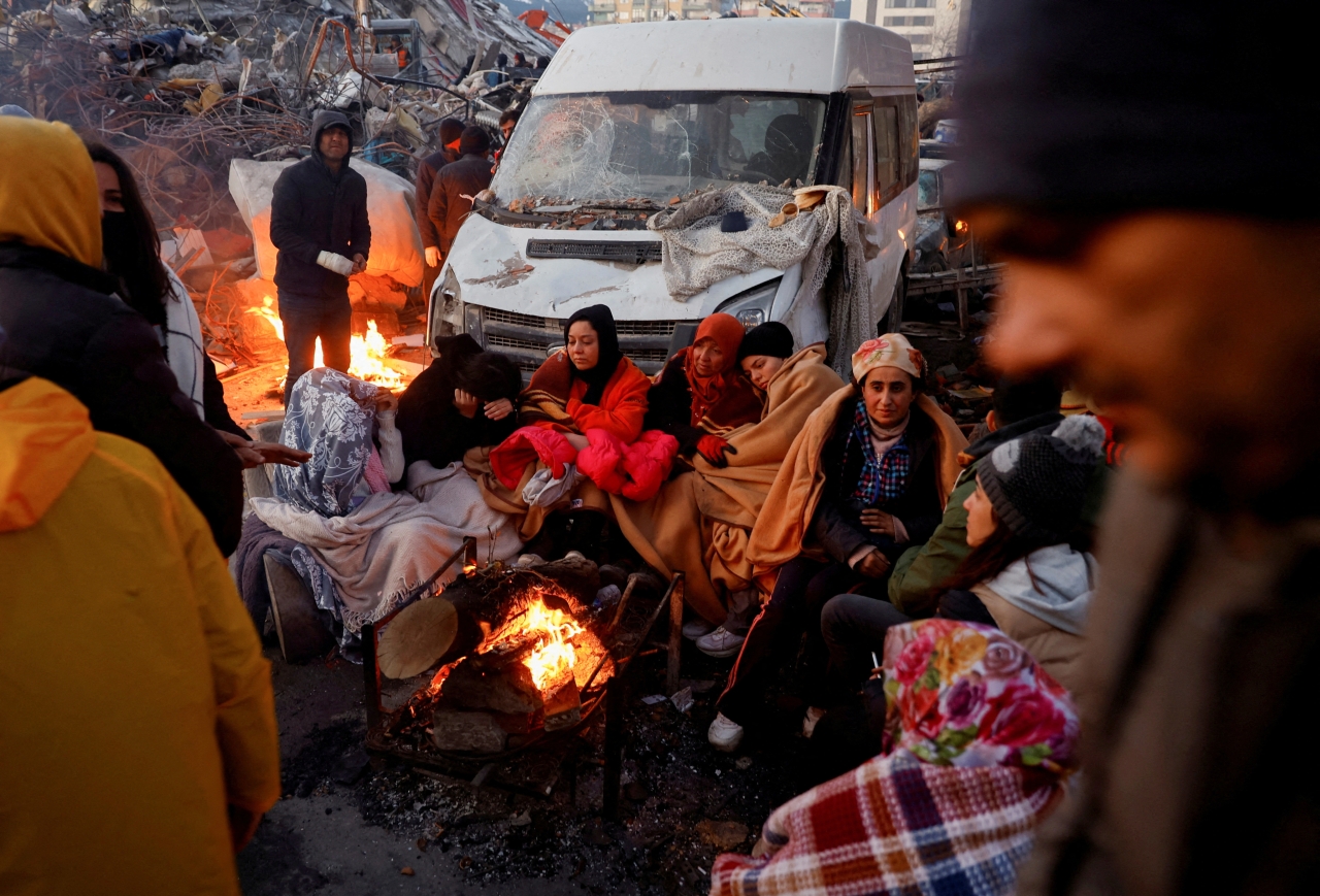 People huddled around a fire amid rubble of collapsed buildings after the earthquake